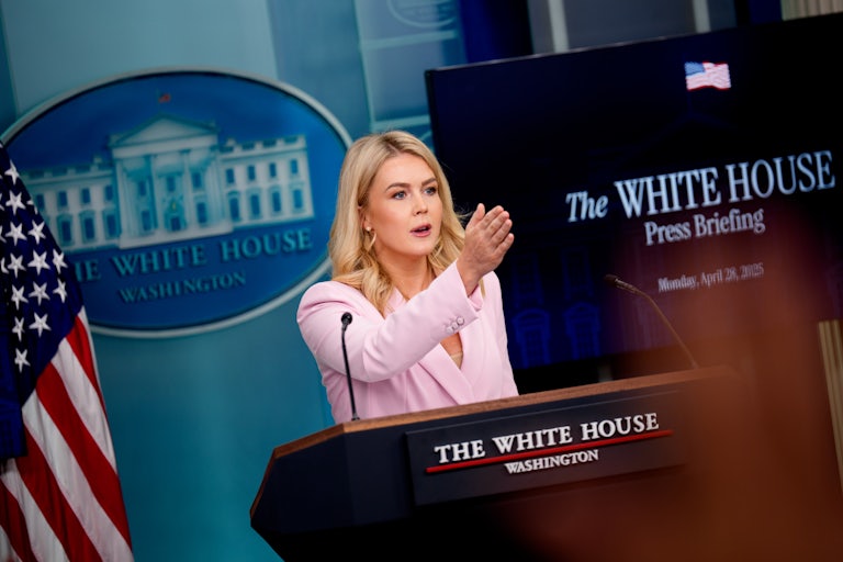 Karoline Leavitt points to someone while standing at the podium in the White House press briefing room.