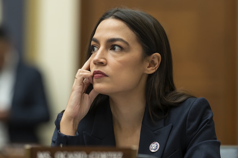 Representative Alexandria Ocasio-Cortez, in a congressional hearing, rests her head on her hand as if thinking