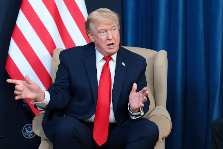 Donald Trump speaking while sitting in front of a U.S. flag