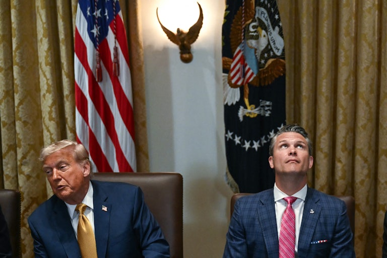 Donald Trump speaks to someone to the side while sitting next to Pete Hegseth, who looks up, during a Cabinet meeting