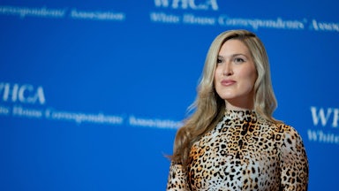 Olivia Nuzzi is shown from the waist up in an animal-print garment in front of a blue background.