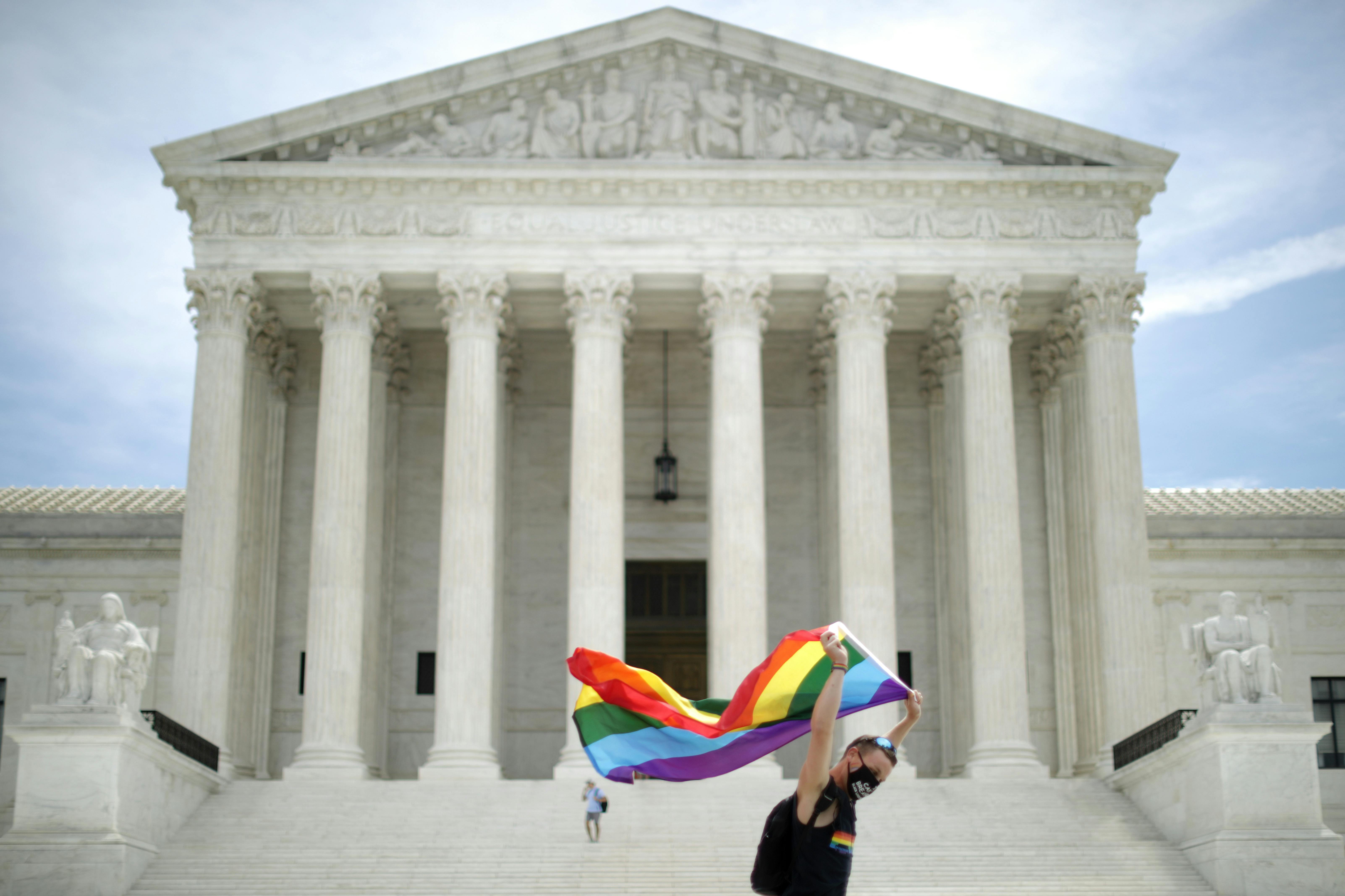 A man holding a Pride Flag walks back and forth in front of the U.S. Supreme Court building.