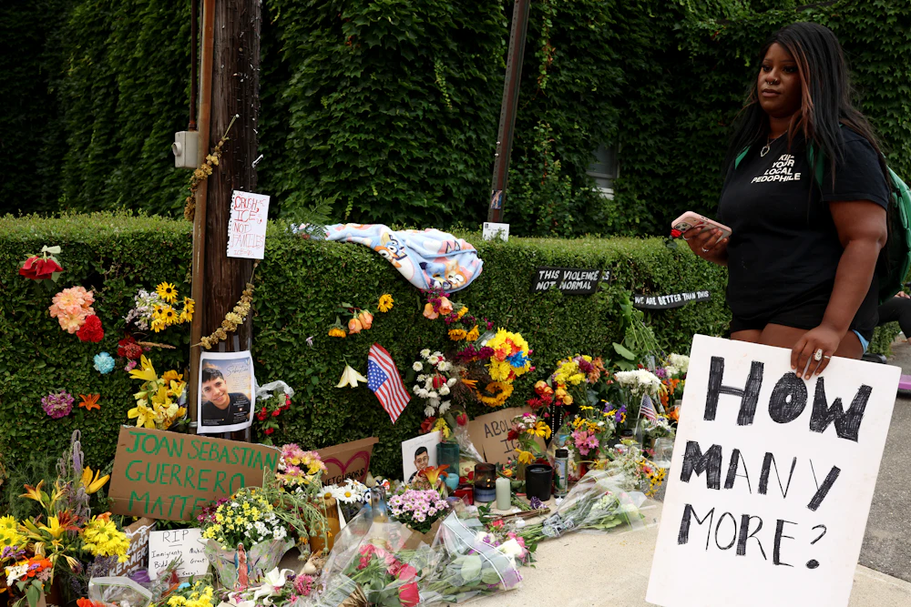 A woman holding a sign that reads "How many more?" visited a memorial for Joan Sebastián Durán Guerrero, who was killed by ICE agents in Biddeford, Maine, on July 13.