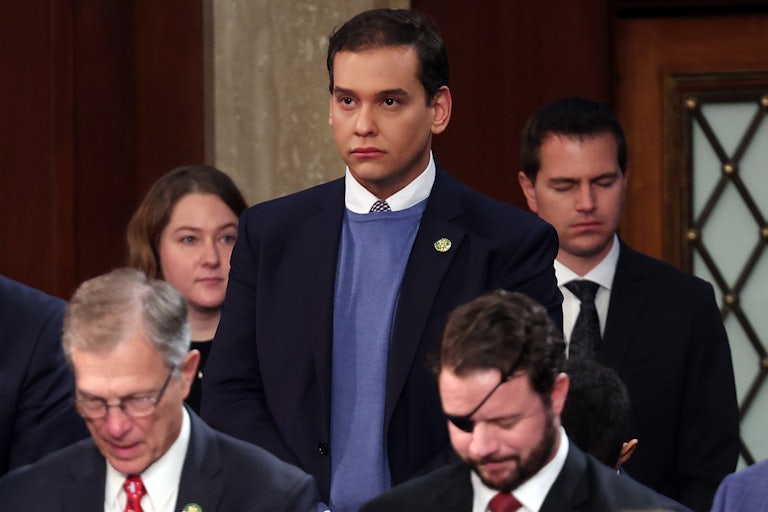 Representative George Santos stands in the House chamber, looking sullen.