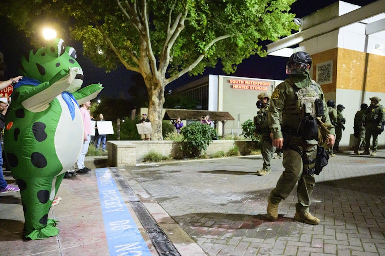A person in an inflatable frog costume stands next to a federal agent