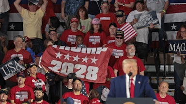 Several people in a crowd hold a flag that reads "Trump 2028" as Trump speaks.