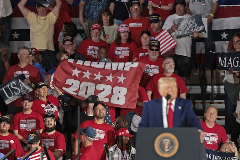 Several people in a crowd hold a flag that reads "Trump 2028" as Trump speaks.