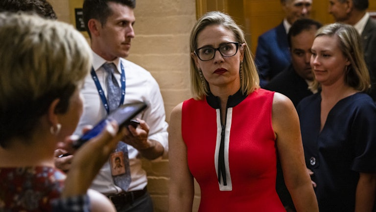 A grimacing Kyrsten Sinema is confronted by reporters.