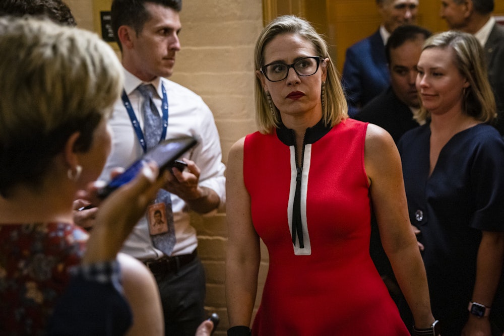 A grimacing Kyrsten Sinema is confronted by reporters.