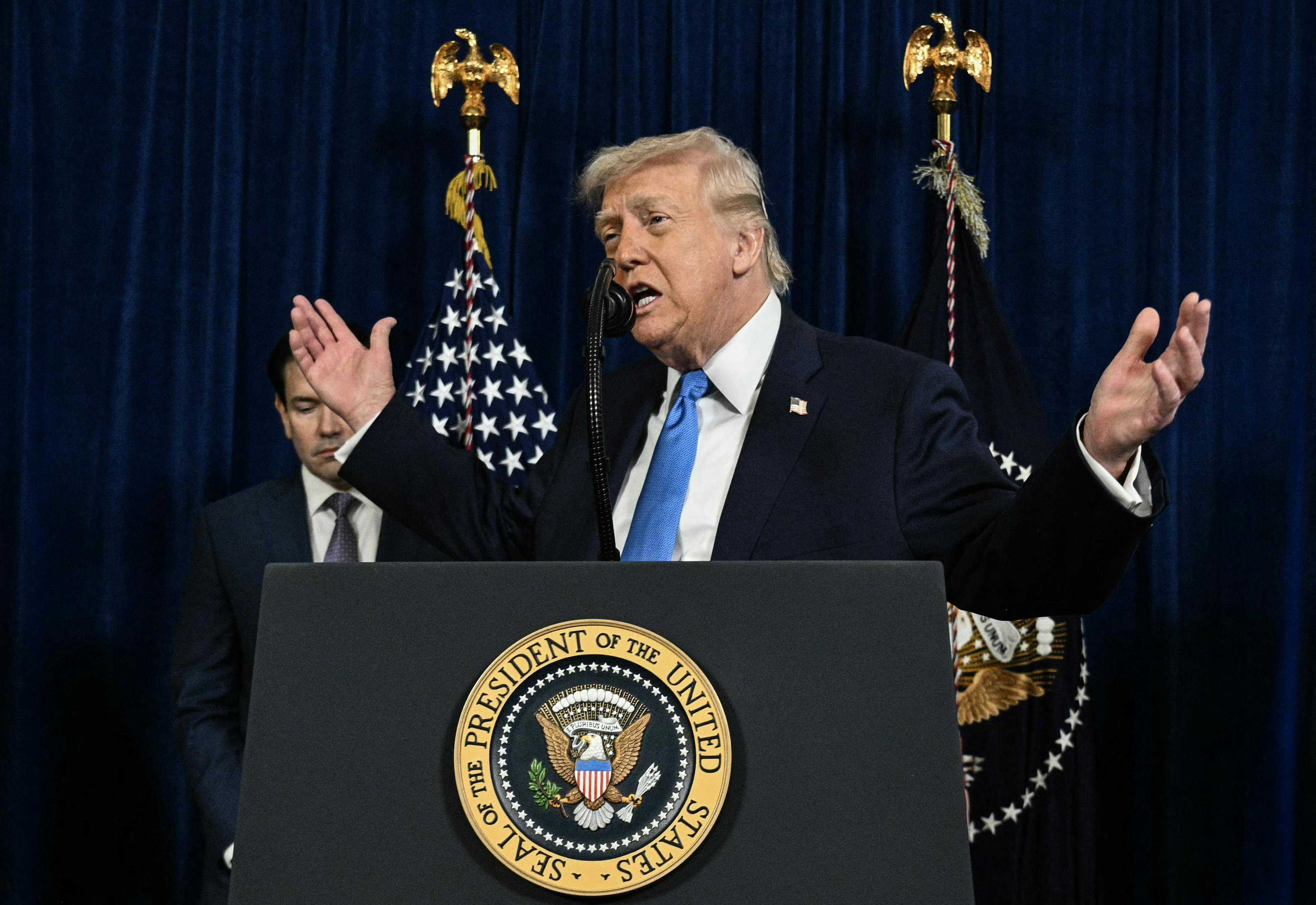 Trump holds his hands out wide while standing behind a podium