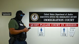 A masked agent looks at his phone in immigration court.
