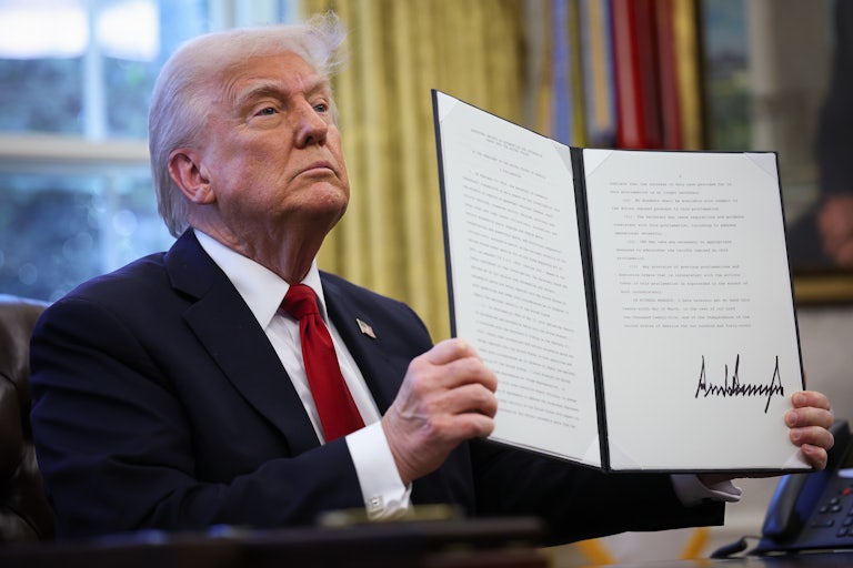 Donald Trump holds up a signed executive order while sitting in the Oval Office