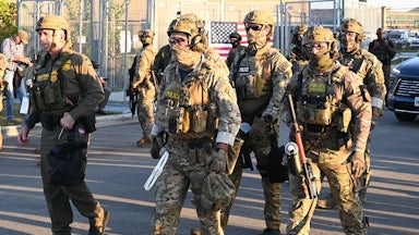 Immigration and Customs Enforcement (ICE) agents, Department of Homeland Security personnel, and Border Patrol Commander Gregory Bovino stand together. Everyone is masked but Bovino.