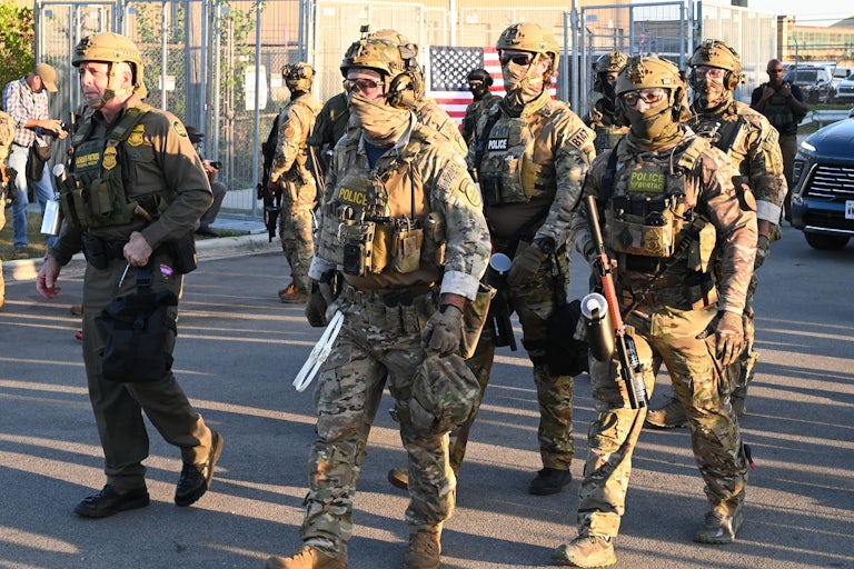 Immigration and Customs Enforcement (ICE) agents, Department of Homeland Security personnel, and Border Patrol Commander Gregory Bovino stand together. Everyone is masked but Bovino.
