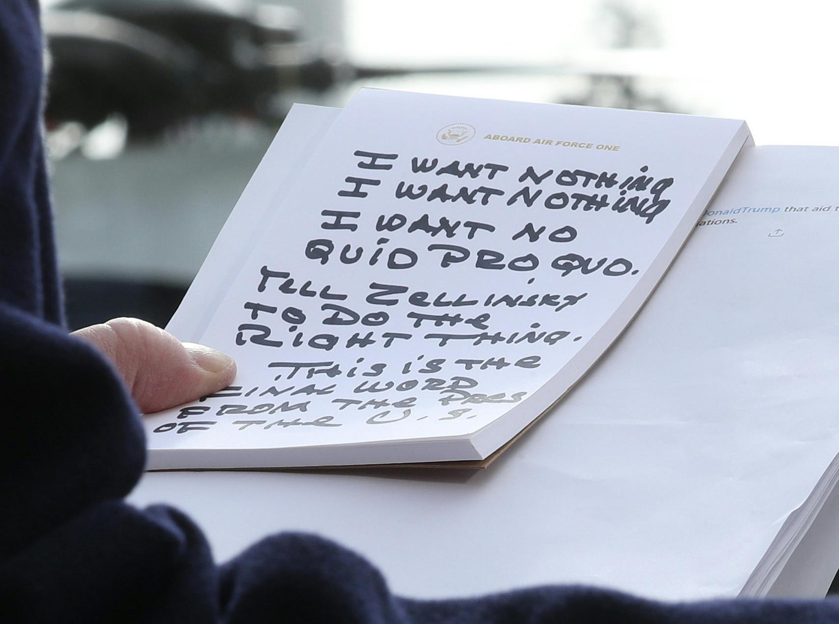 Donald Trump clutching a notepad with “I want nothing” and “I want no quid pro quo” written on it in large capitalized letters