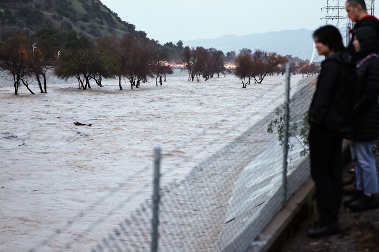 People look over a fence at the swollen Los Angeles River.