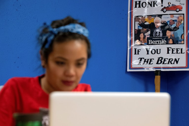 A volunteer works on a laptop in front of a Bernie Sanders campaign sign.