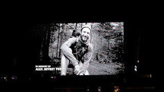 Black and white photo of Alex Pretti hiking in the woods appears on a large screen with the words "In memory of Alex Jeffrey Pretti"