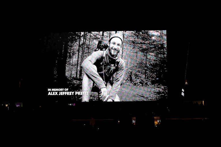 Black and white photo of Alex Pretti hiking in the woods appears on a large screen with the words "In memory of Alex Jeffrey Pretti"