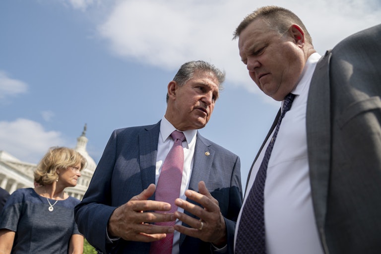 Senators Joe Manchin and John Tester speak outside. The Capitol is in the background.