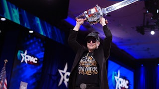 Elon Musk holds a chainsaw over his head and smiles at CPAC.