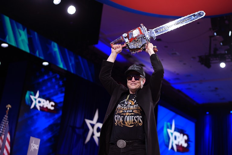 Elon Musk holds a chainsaw over his head and smiles at CPAC.
