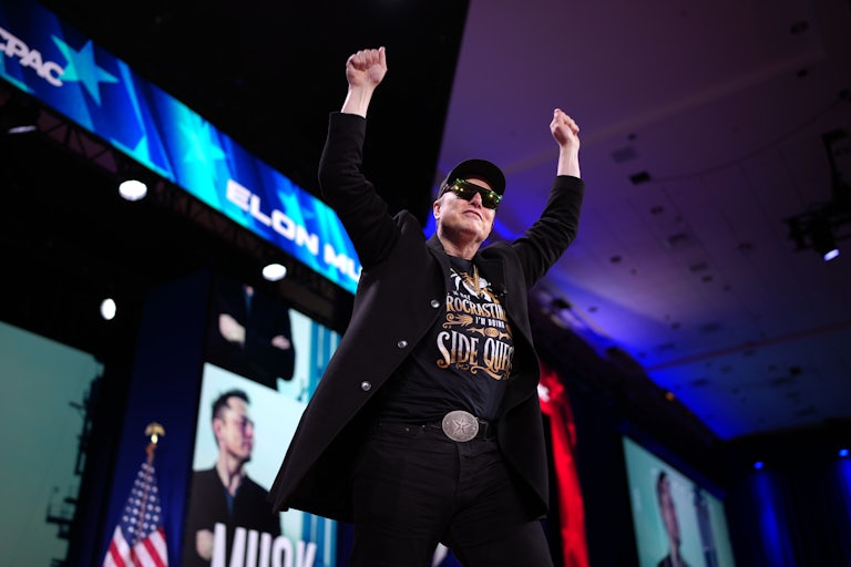 Elon Musk holds his fists above his head while onstage at CPAC