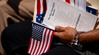 A hand holds onto a U.S. flag and a printed piece of paper with the lyrics of The Star-Spangled Banner.