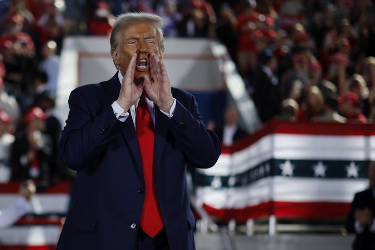Donald Trump holds his hands up to his mouth while he yells during a campaign rally