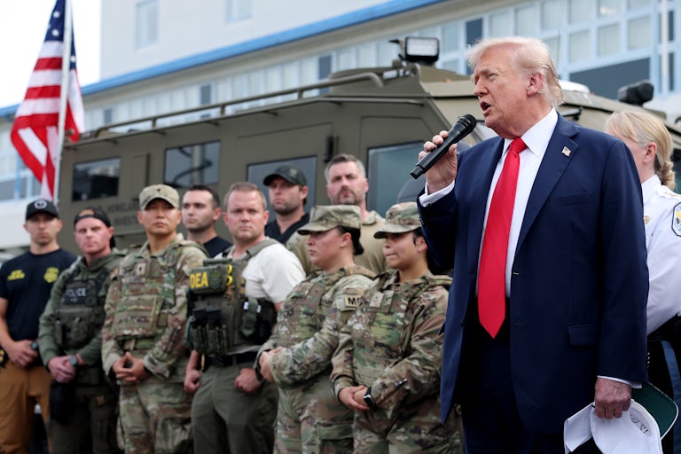 Trump stands with National Guard troops as he speaks in a mic.