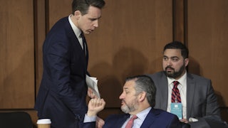 Josh Hawley bends down to talk to Ted Cruz, seated, who holds up a clenched fist