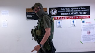 A white man wearing glasses, a face mask, and an ICE vest walks as he looks directly at the camera.