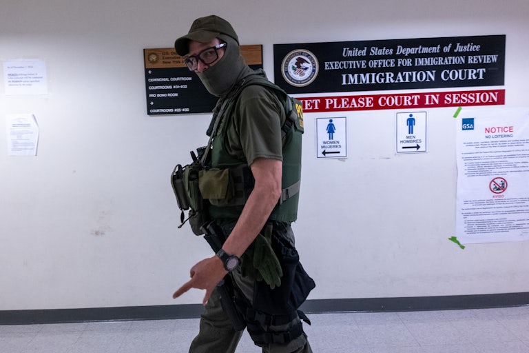 A white man wearing glasses, a face mask, and an ICE vest walks as he looks directly at the camera.