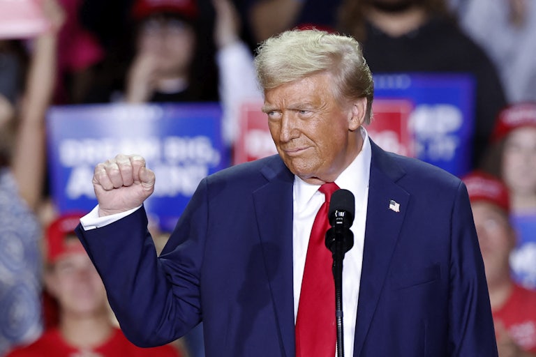 Donald Trump holds up a fist while standing in front of a microphone