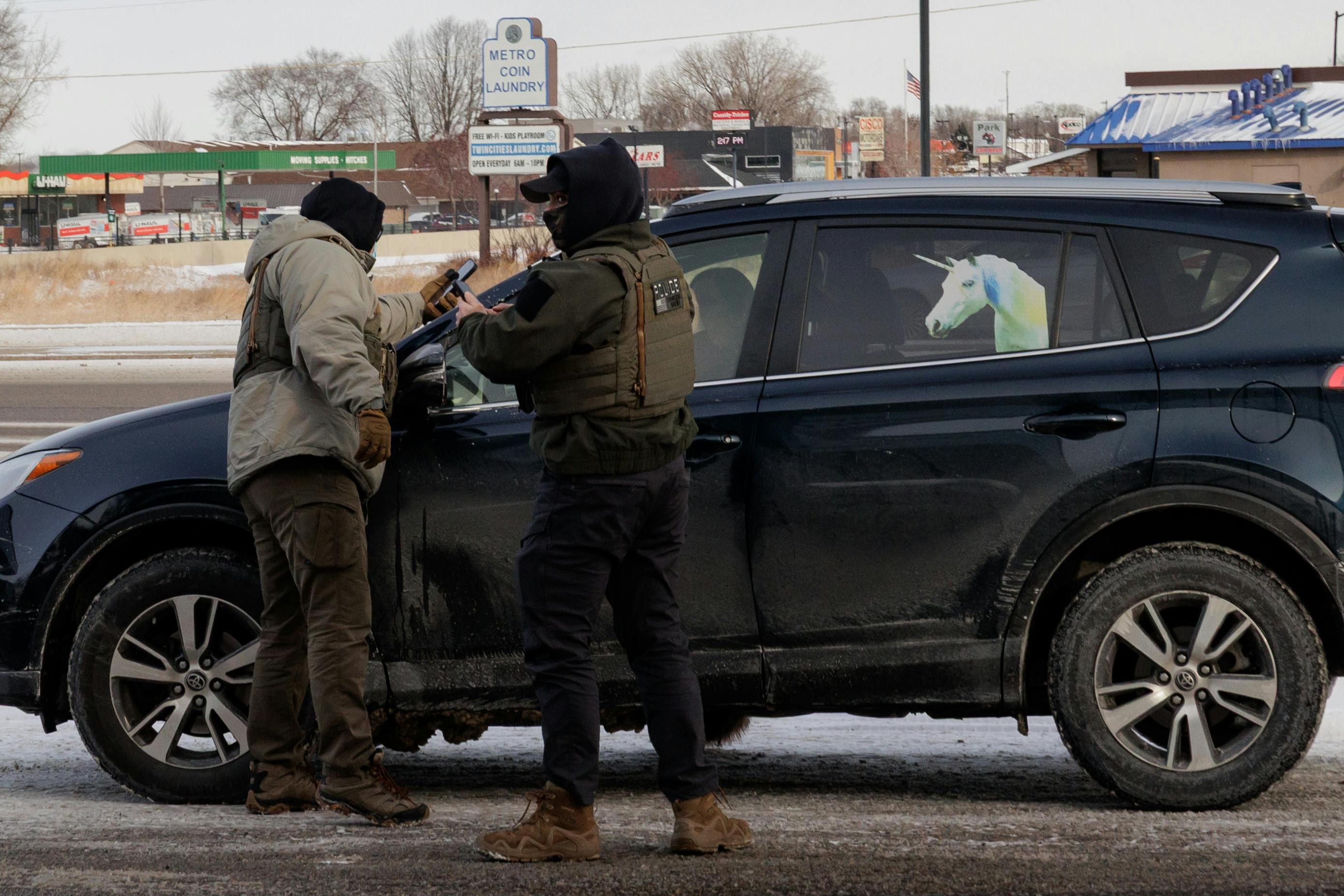 Federal immigration agents stand outside a car with a unicorn on it.