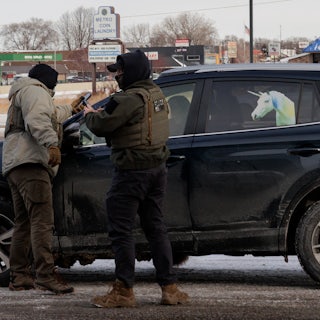 Federal immigration agents stand outside a car with a unicorn on it.