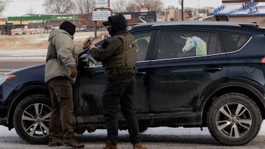 Federal immigration agents stand outside a car with a unicorn on it.
