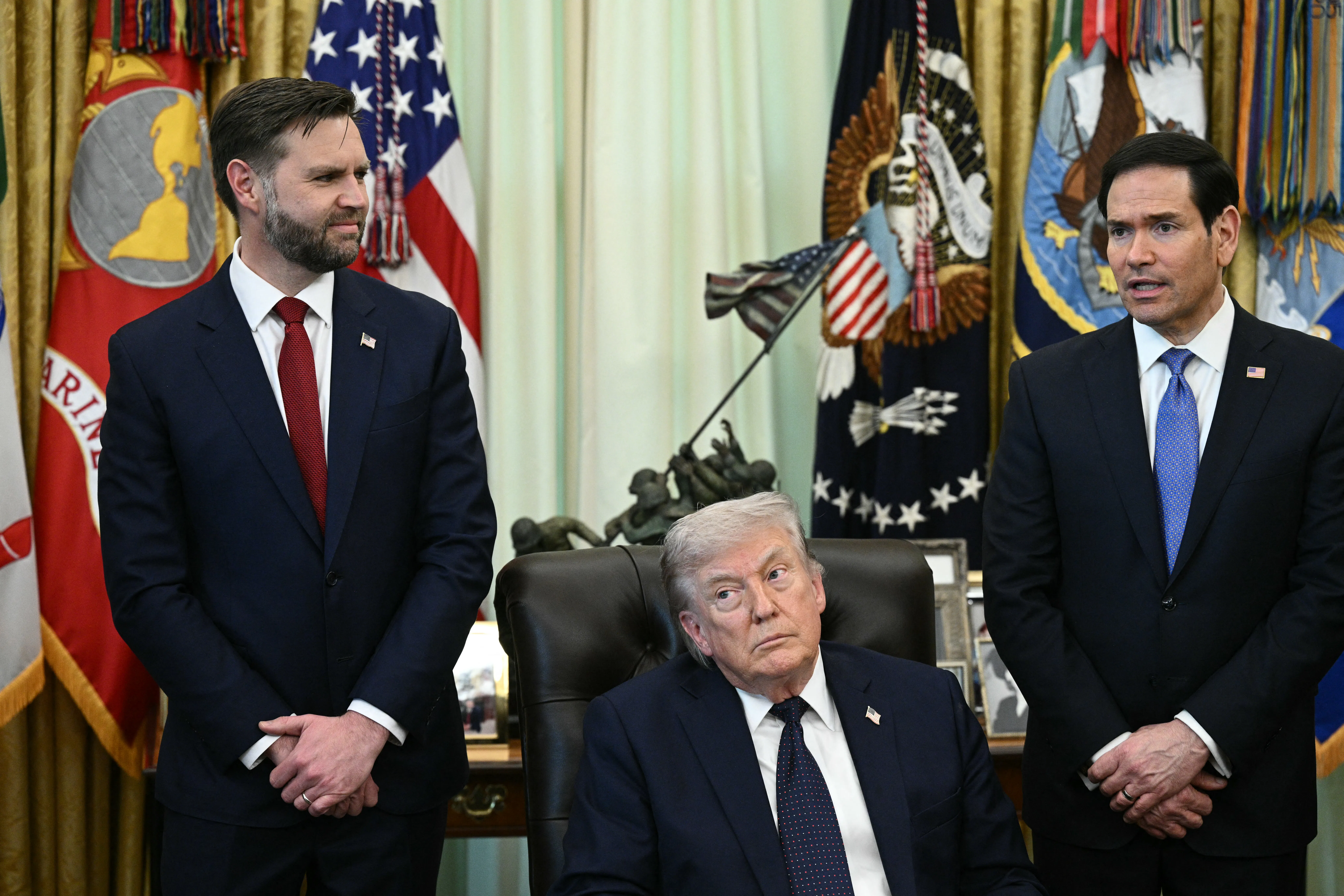 President Donald Trump sits at his desk in the Oval Office, while Vice President JD Vance and Secretary of State Marco Rubio stand behind him.