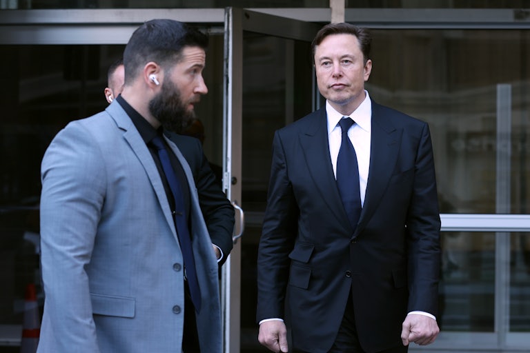 Elon Musk walks out of a building, as a bodyguard stands nearby