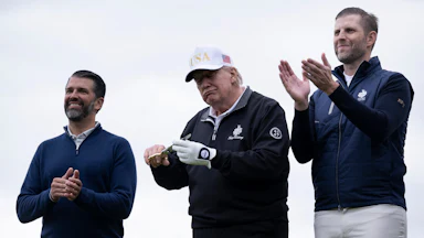 Donald Trump Jr. and Eric Trump clap and smile while flanking their father on a golf course