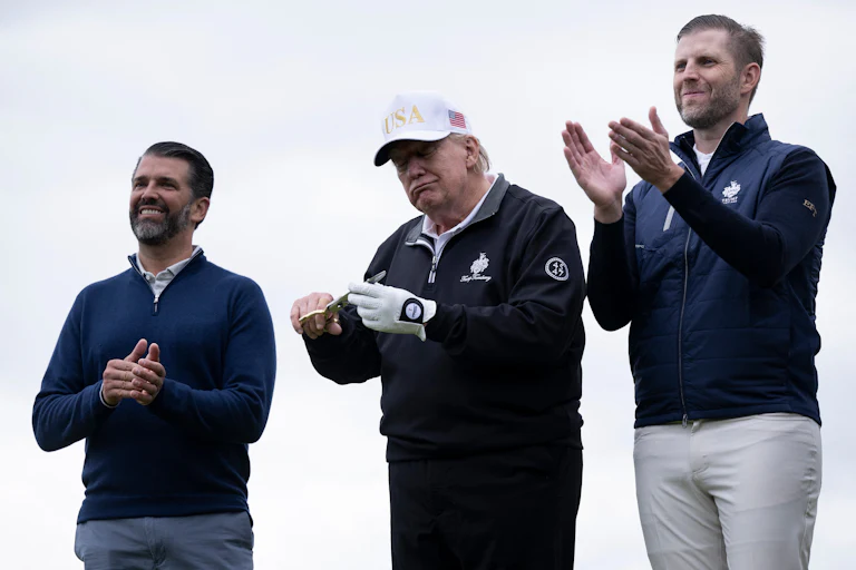Donald Trump Jr. and Eric Trump clap and smile while flanking their father on a golf course