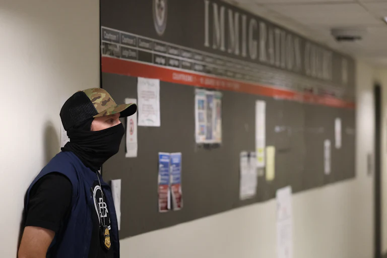 A masked federal agent waits outside the immigration court in New York