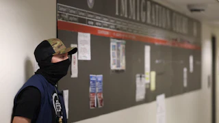 A masked federal agent waits outside the immigration court in New York