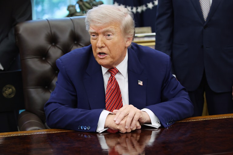 Donald Trump speaks and rests his hands on his desk in the Oval Office of the White House.