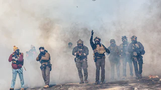 heavily armed federal agents walk through tear gas they've deployed in minnesota