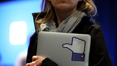 A Facebook employee holds a laptop with a "like" sticker on it.