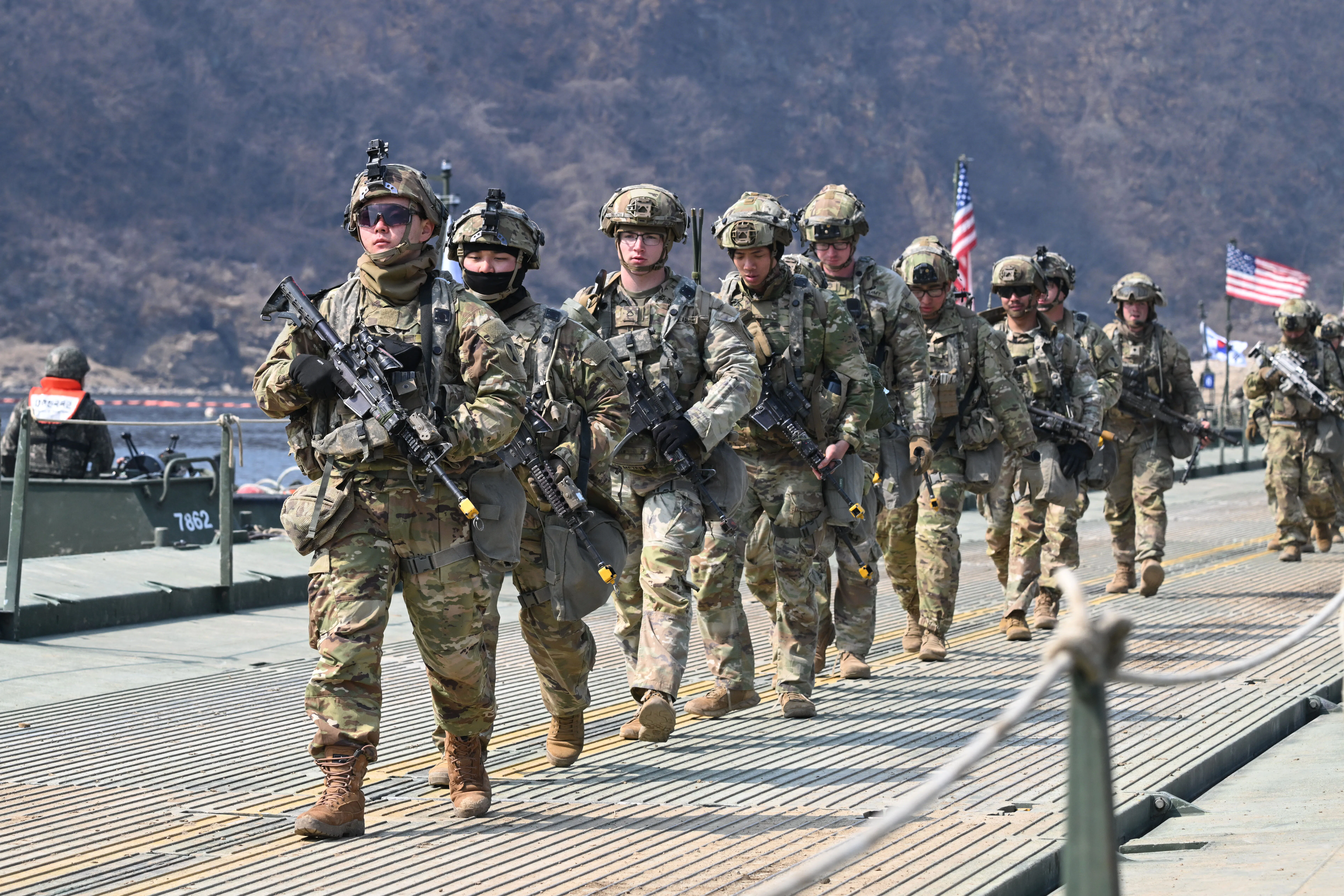 U.S. troops carrying guns walk in a single-file line