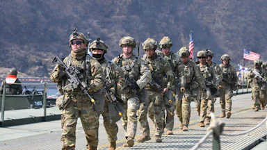 U.S. troops carrying guns walk in a single-file line