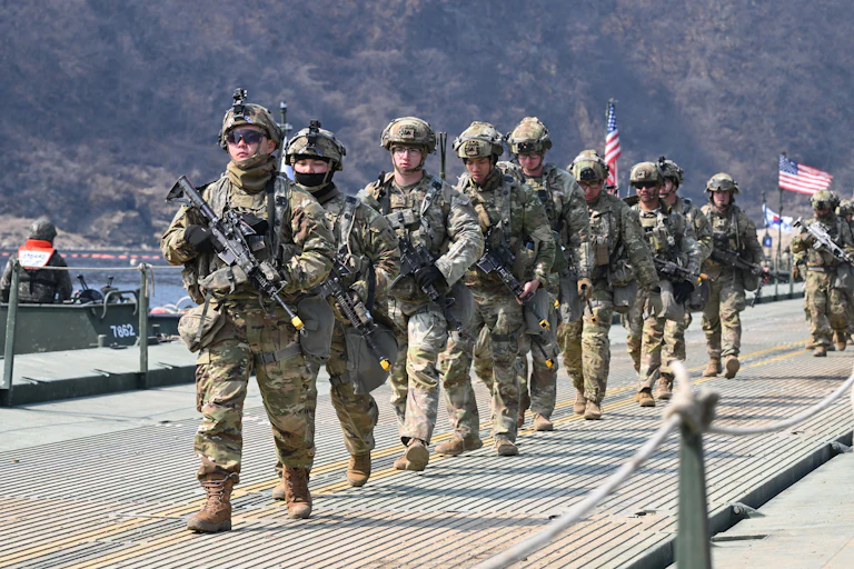 U.S. troops carrying guns walk in a single-file line