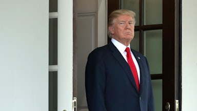 A glowering President Donald Trump stands in the door of the White House.